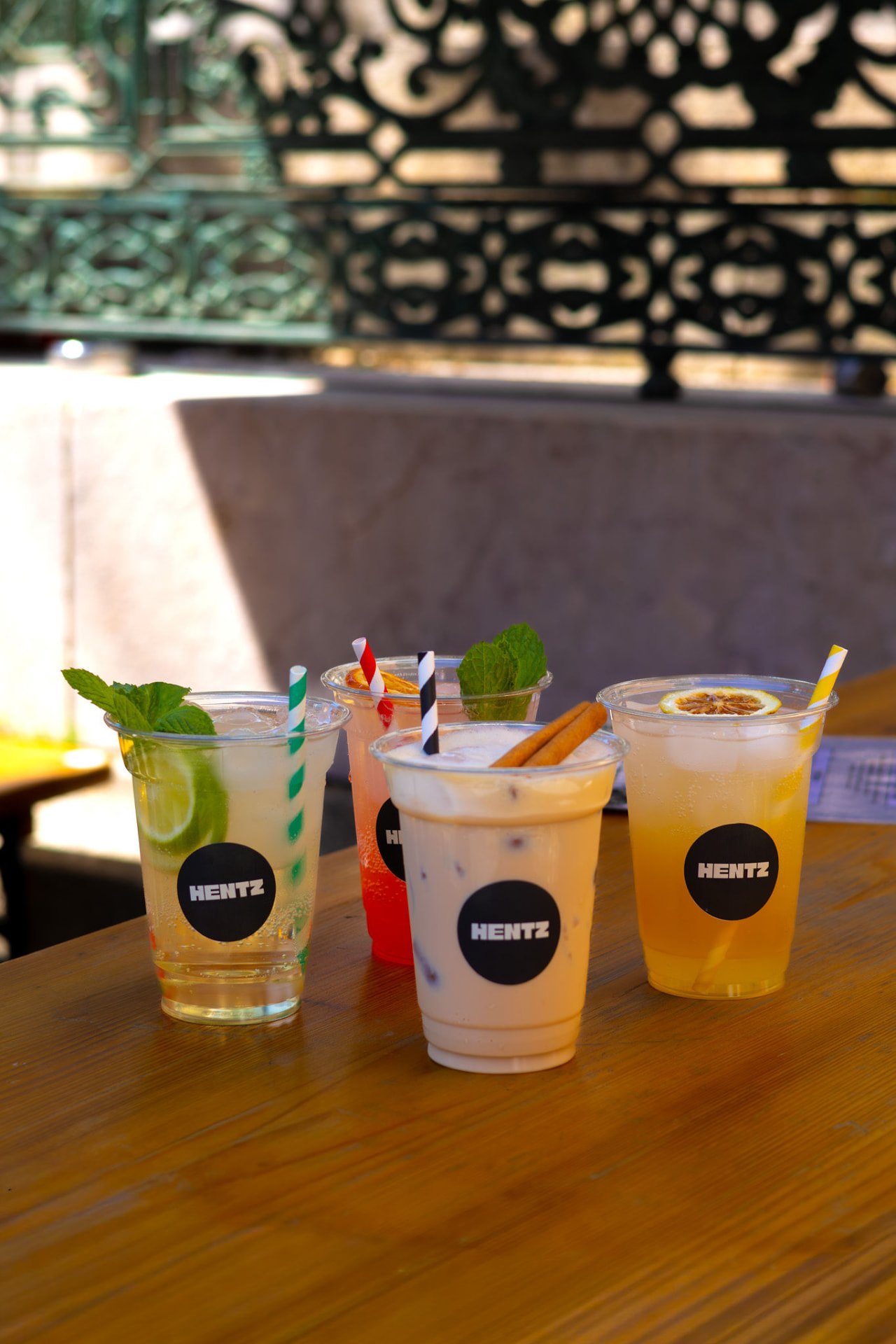 Quatro cocktails HENTZ em copos de take-away sobre uma mesa de madeira